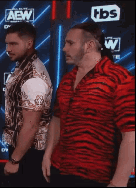 two men standing in front of a aew logo