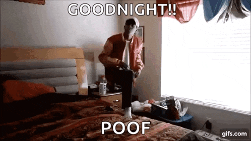 a man in a red jacket is sitting on a bed with a video game controller in his hand .