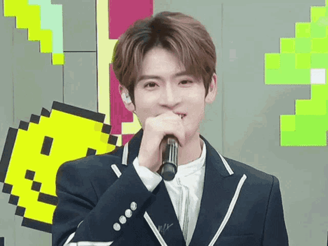 a young man in a suit is holding a microphone in front of his mouth .