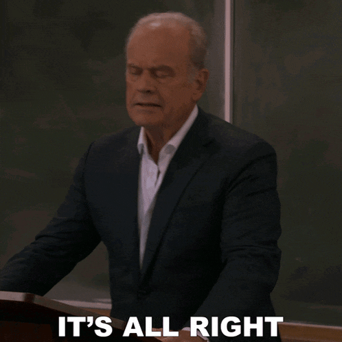a man in a suit says it 's all right in front of a chalkboard