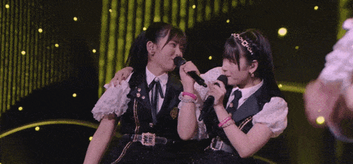 two girls are singing into microphones on a stage and one has a tiara on her head