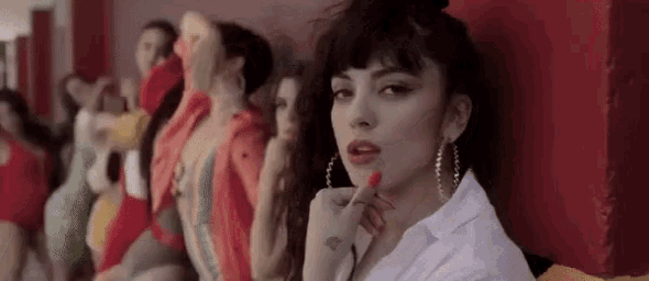 a woman with red lipstick and hoop earrings is sitting in front of a group of dancers .