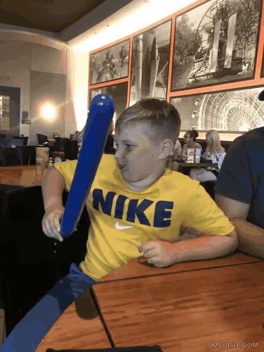 a young boy wearing a yellow nike shirt holds a blue balloon bat