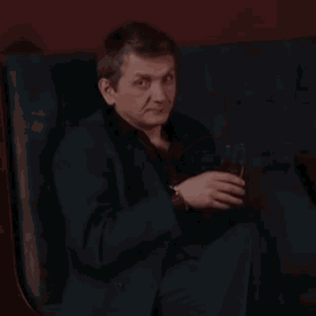 a man in a blue suit is sitting on a couch holding a glass