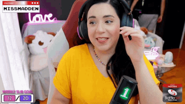 a woman wearing headphones and a yellow shirt is sitting in front of a screen that says missmadden