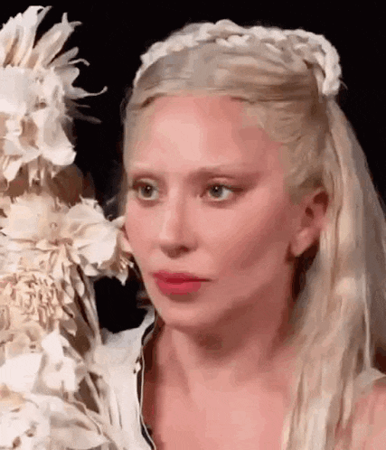 a woman with blonde hair and a braided headband is standing next to a wedding cake .