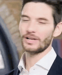 a close up of a man with a beard wearing a suit and white shirt with his eyes closed .