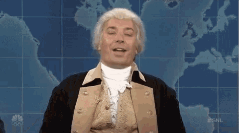 a man in a wig is standing in front of a map of the world and talking .