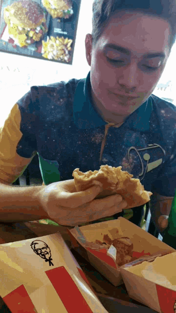 a man in a galaxy shirt is eating a kfc meal