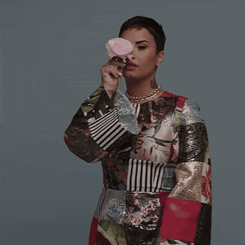 a woman in a patchwork dress is holding a pink rose in her hand