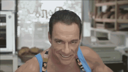a muscular man wearing a blue tank top is smiling in a kitchen .