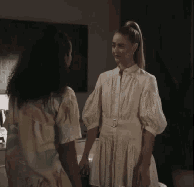 a woman in a white dress is standing next to another woman