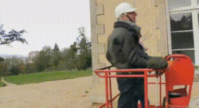 a man wearing a hard hat is standing in a bucket on a lift .
