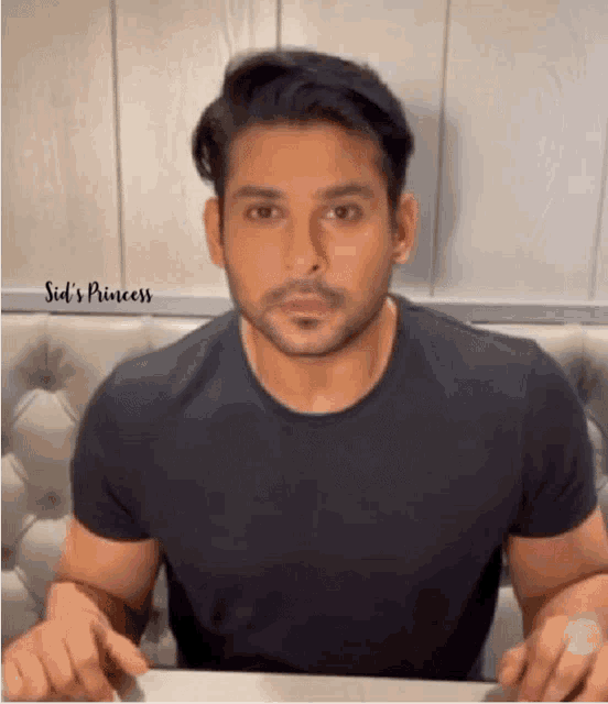a man in a black t-shirt is sitting at a table and making a funny face .