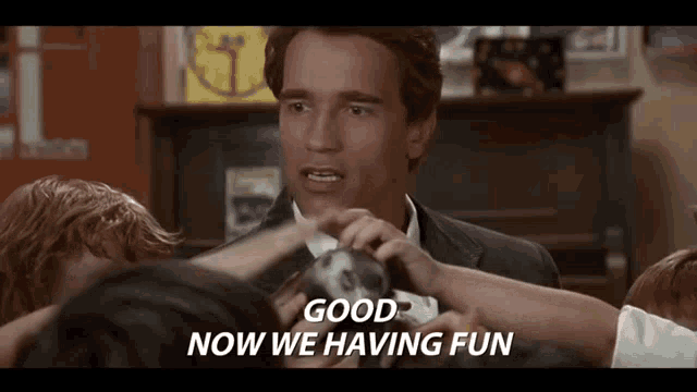 a man in a suit is surrounded by children and says `` good now we 're having fun '' .