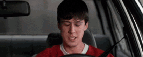 a young man in a red shirt is driving a car and making a funny face .