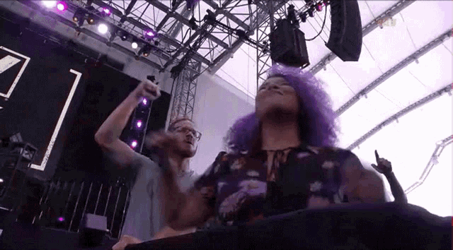 a woman with purple hair and a man with glasses are dancing on stage