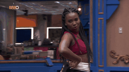 a woman with braids is standing in front of a blue wall in a kitchen .