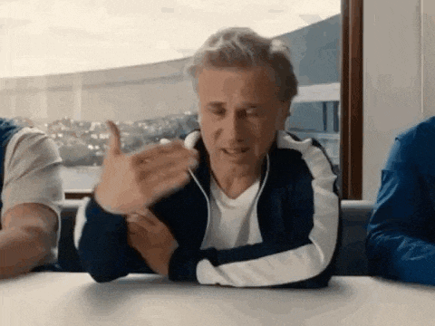a man is sitting at a table with his hands outstretched and talking to another man .