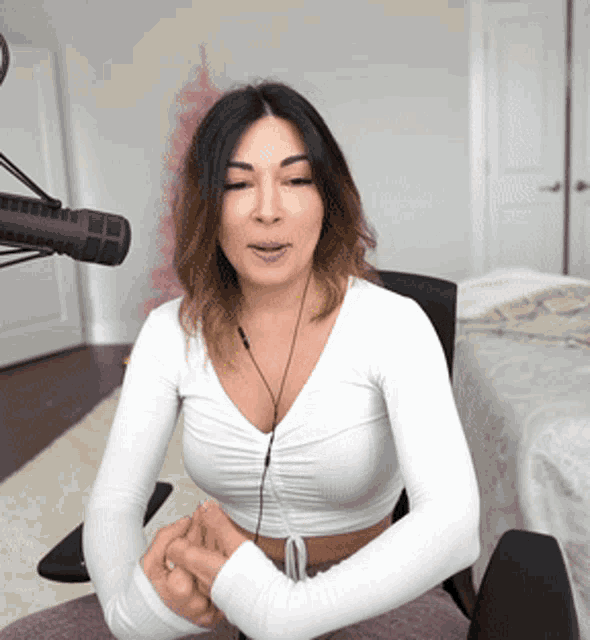 a woman is sitting in front of a microphone wearing a white crop top
