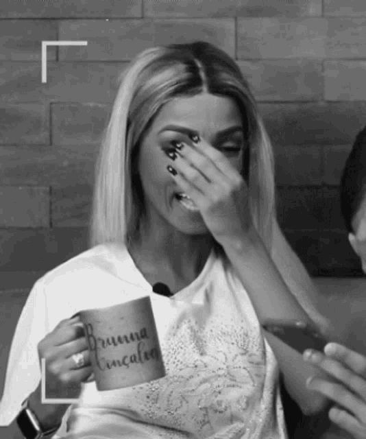 a woman covering her face while holding a coffee mug that says brunna