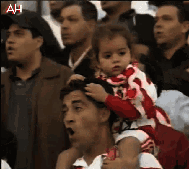 a man is carrying a little girl on his shoulders in a crowd with ah written on the bottom