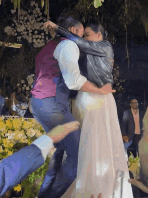 a bride and groom are kissing in front of a table of yellow roses