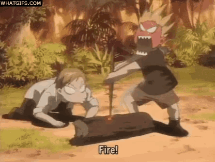 a man is laying on the ground while another man is standing next to a log with a stick in it .