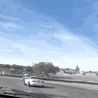 a white car is driving down a highway with a blue car in the background .