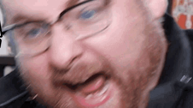 a man with glasses and a beard is making a funny face with his mouth open .