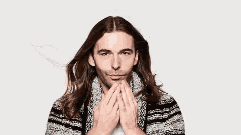 a man with long hair and a beard is smiling and wearing a sweater .