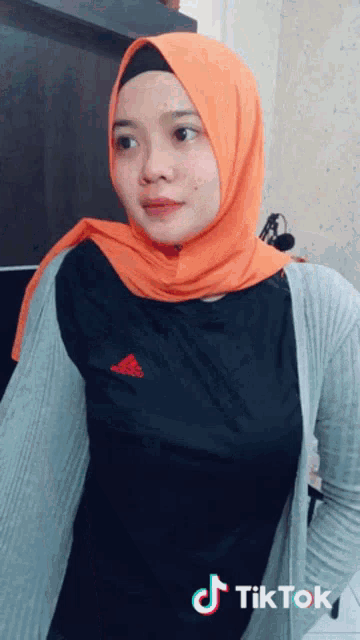a woman wearing an orange hijab and a black shirt with the word adidas on the front