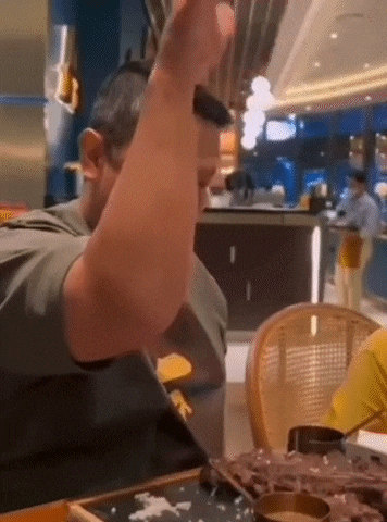 a man is sitting at a table in a restaurant holding a tray of food in his hand .