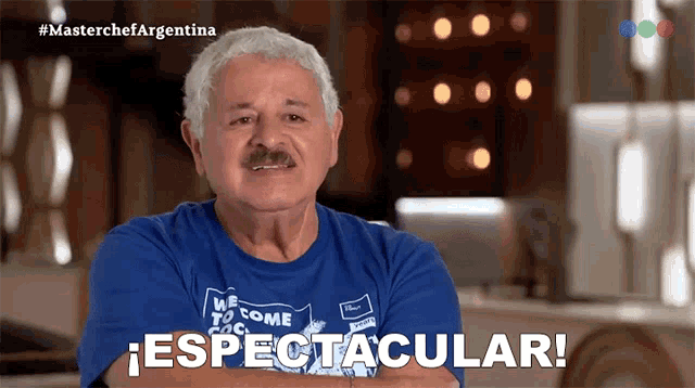 a man wearing a blue shirt that says " espectacular " stands with his arms crossed