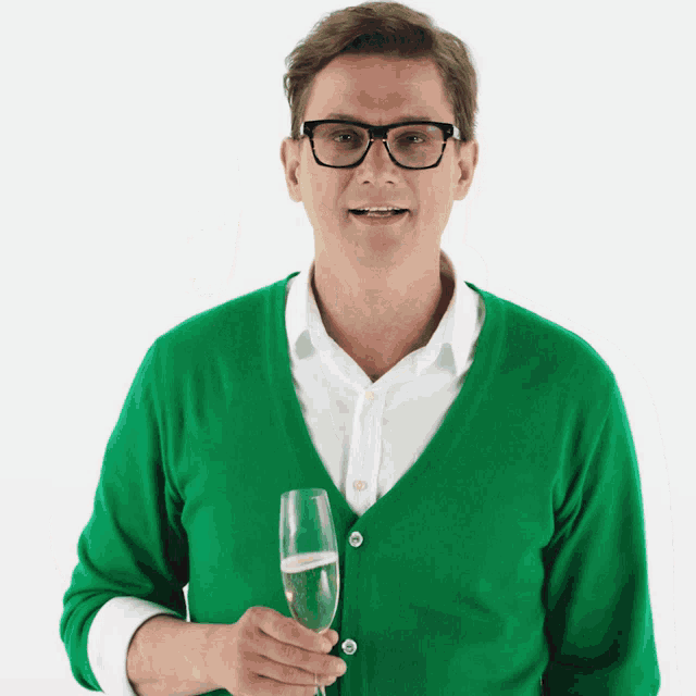 a man in a green sweater and glasses holds a glass of champagne