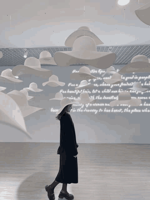 a woman stands in front of a wall with a lot of white hats hanging from the ceiling