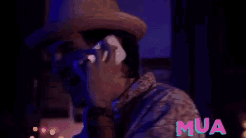 a man wearing a straw hat is talking on a cell phone in a dark room .