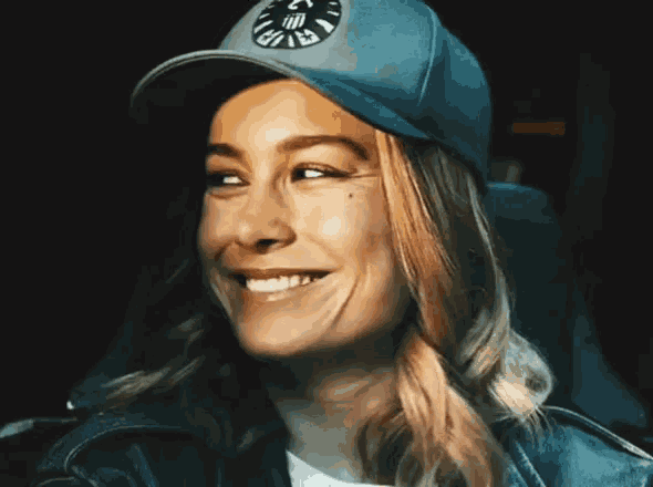 a woman wearing a hat with a shield logo on it is smiling