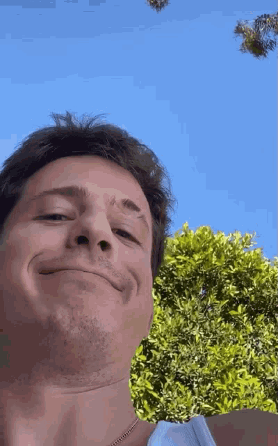 a close up of a man 's face against a blue sky with trees in the background