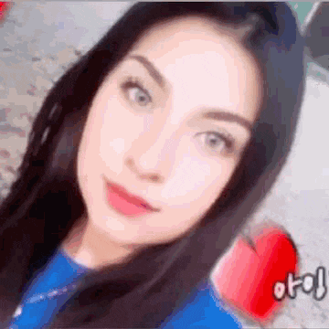 a woman in a blue shirt is taking a selfie with a red heart .
