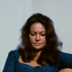 a woman with long brown hair is wearing a blue polka dot dress and looking down .