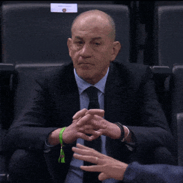 a bald man in a suit and tie sits in a stadium