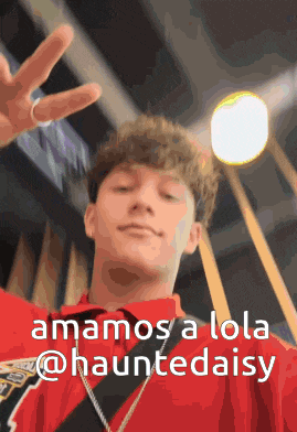 a young man in a red shirt is giving a peace sign with the caption " amamos a lola @hauntedaisy "