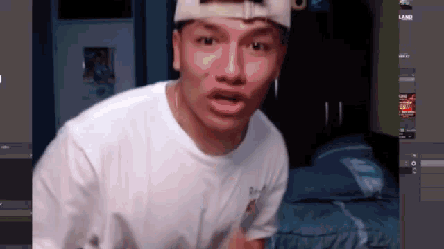 a man wearing a white hat and a white t-shirt is standing in front of a computer screen that says land