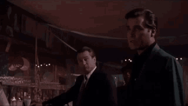 a man in a suit and tie is standing in front of a bar with the word ok on the bottom