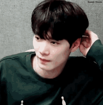 a young man in a green shirt is holding his hand to his ear and looking at the camera .