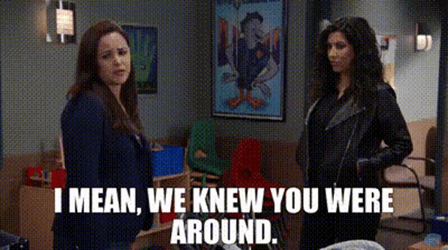 two women are standing next to each other in a room and one of them is saying `` i mean we knew you were around . ''