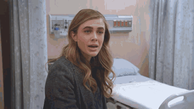 a woman is sitting in a hospital room with a bed in the background and a clock on the wall