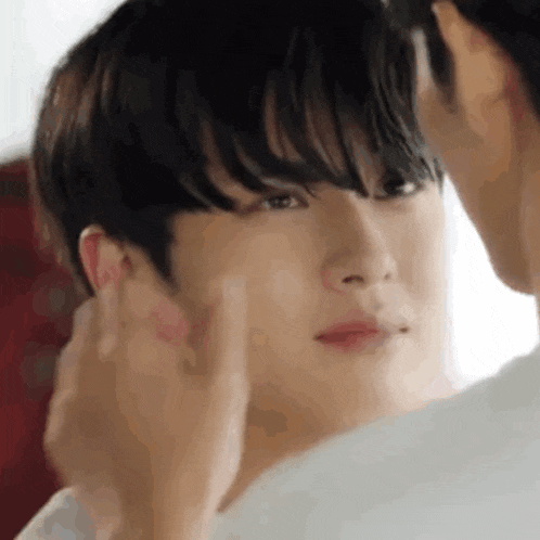 a man is touching another man 's face while looking at him in the mirror .