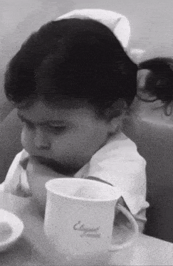 a little girl is sitting at a table with a cup that says elegant on it